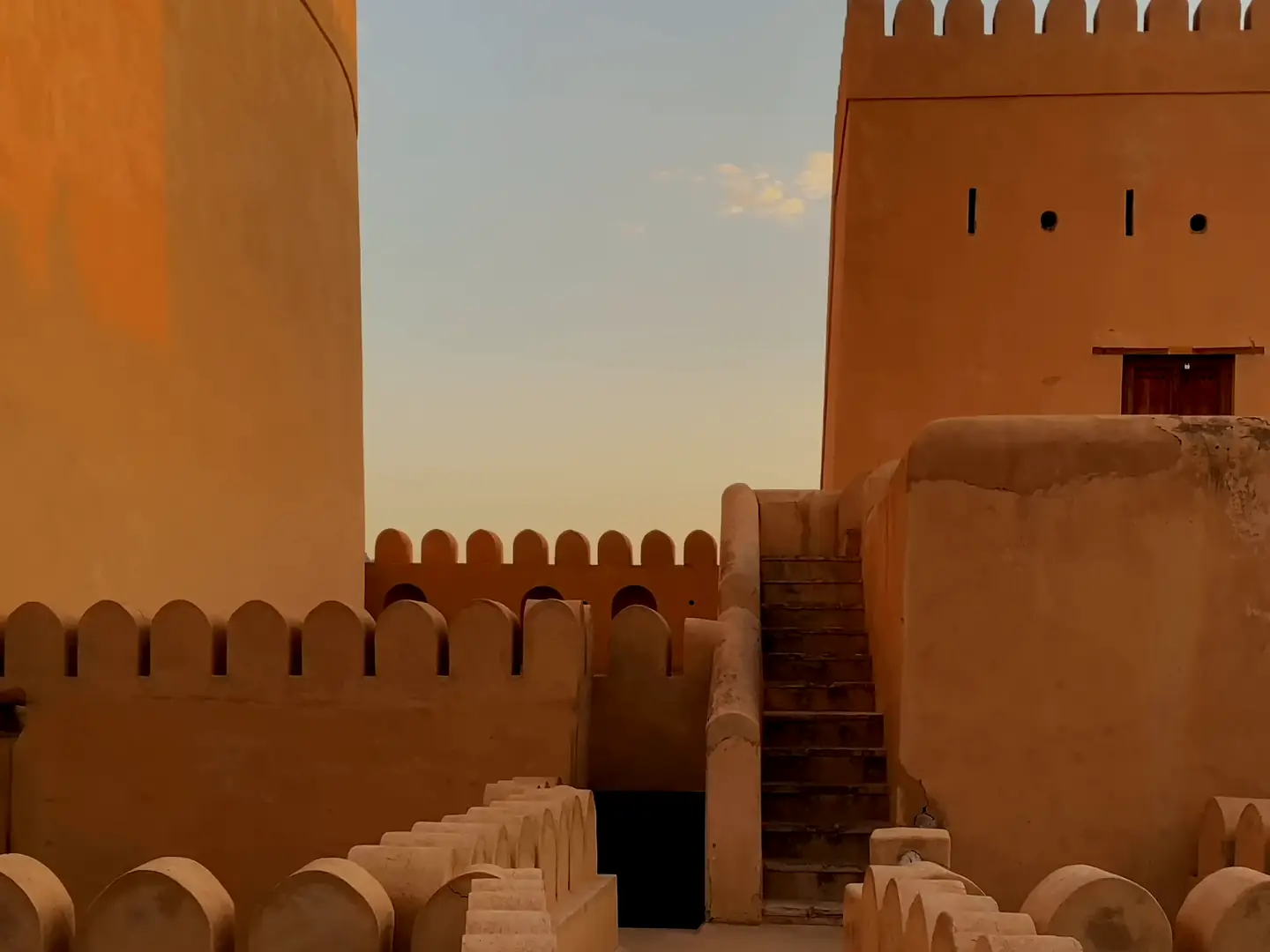 Film walking the battlements of an Omani fort in the evening light, and a valley of date palms and villages at the foot of the Hajar mountains