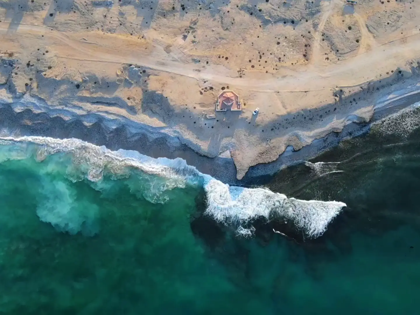 Film of waves breaking under the cliffs of the Dhofar coast, a beach with fishing boats, and khareef mist over green mountains near Salalah