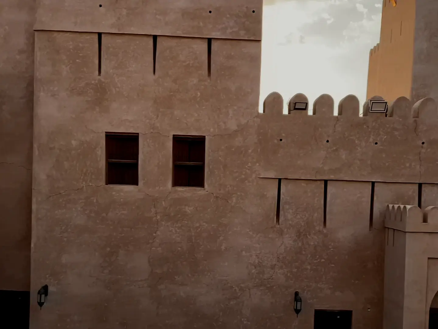 Film of an Omani fort’s towers and gate at sunset, the busy goat market in Nizwa, and an old mud-brick village among palms