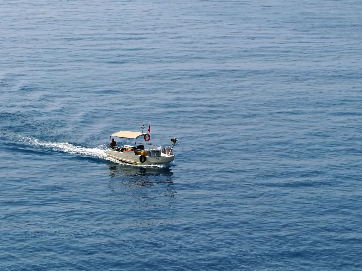 Film of a small boat heading out over deep blue water, an angler reeling in a line from a motor boat, a trolling rod over the wake, and turquoise water on the rocks of the Muscat coast