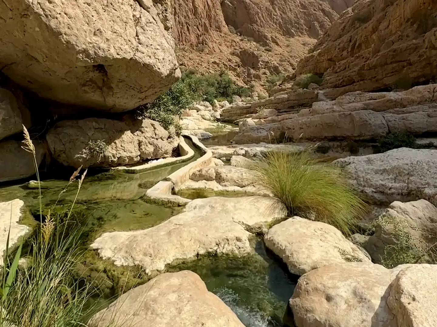 Film of green pools between boulders in an Omani wadi, golden sand dunes in Oman, and 4x4s crossing orange dunes seen from above